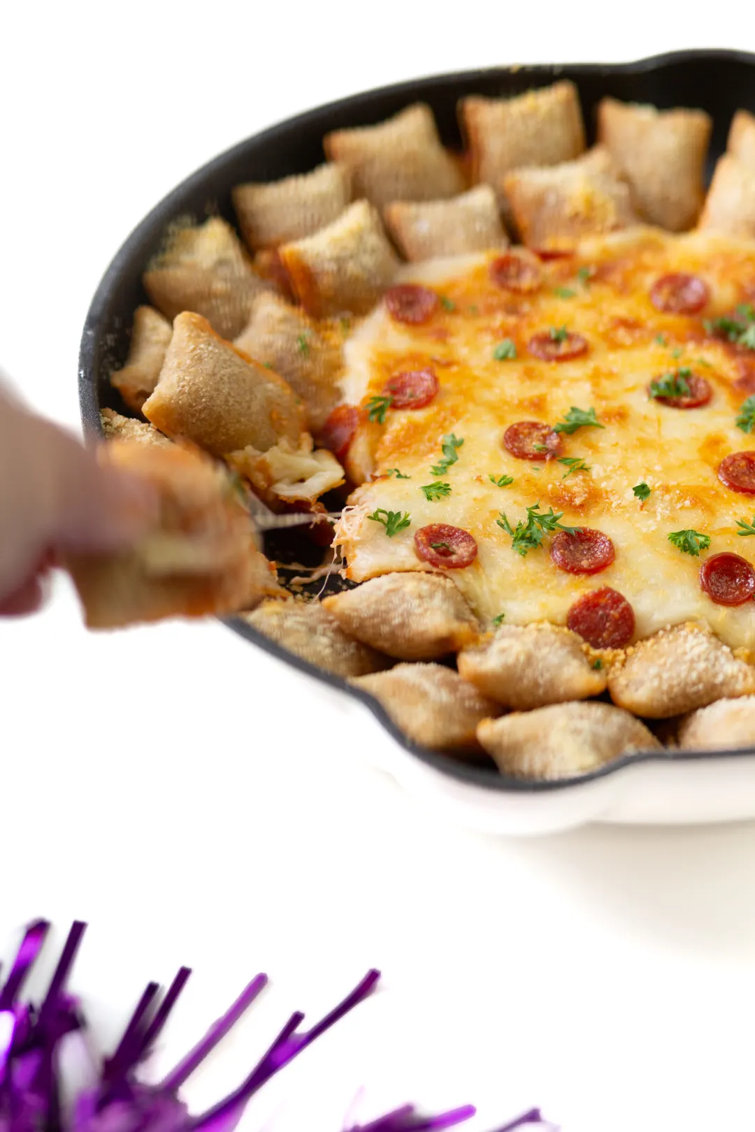 woman grabbing pizza roll from a cheesy pizza dip in a skillet