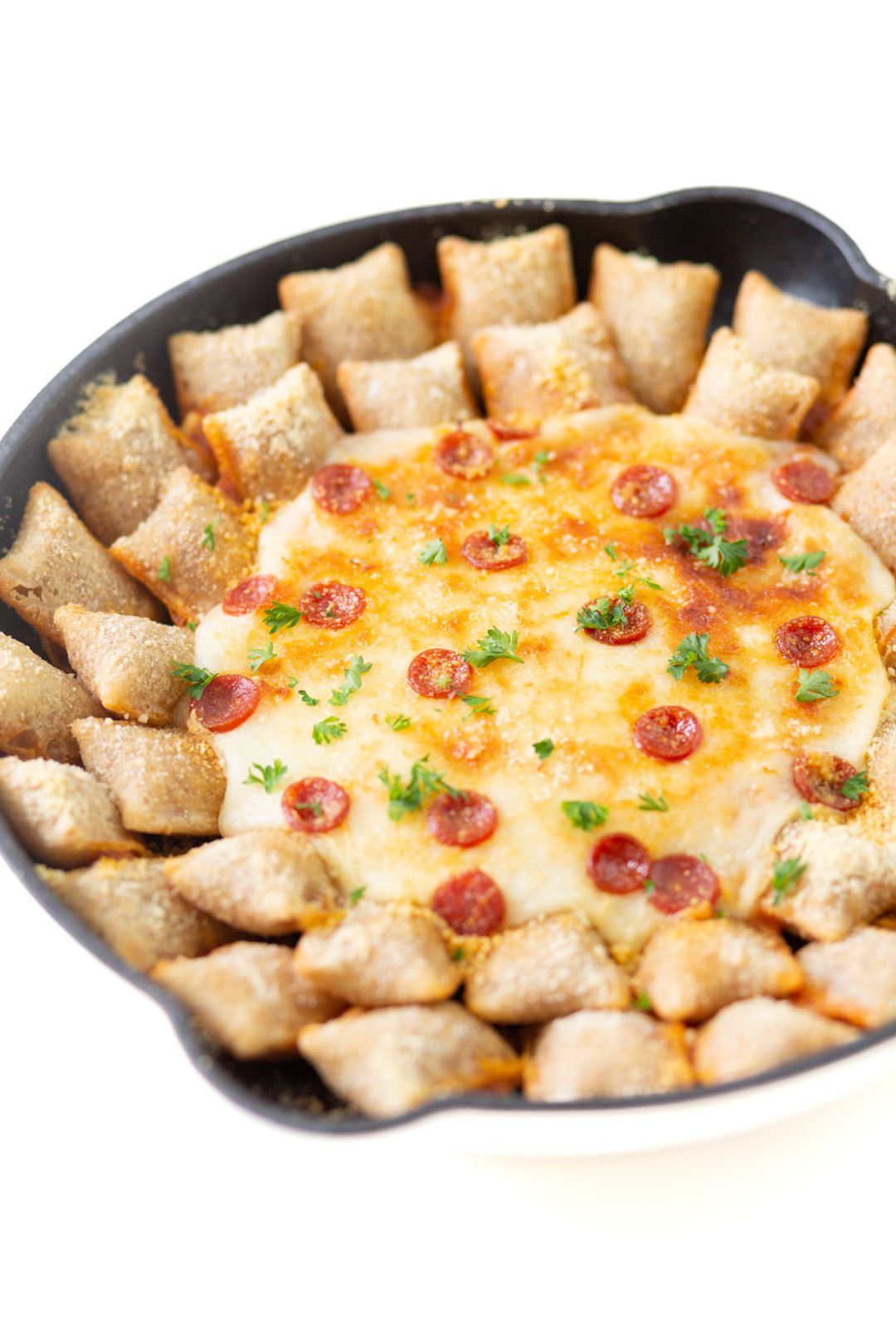 cheesy pepperoni dip up close being served in a skillet with totinos pizza rolls, melted cheese, crispy mini pepperoni and snipped parsley garnish.