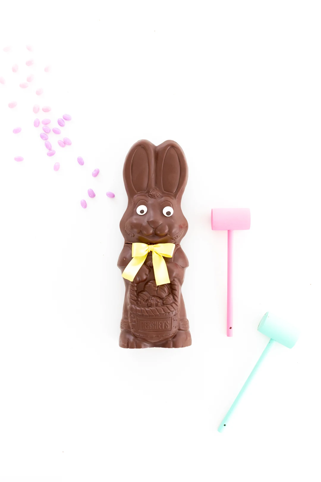 smash chocolate bunny with pastel mini mallets and jelly beans spread on the table.