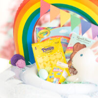 cute pool float easter basket that is rainbow themed, filled with matching items in rainbow colors such as yellow peeps, crayola coloring book, stuffed bunny