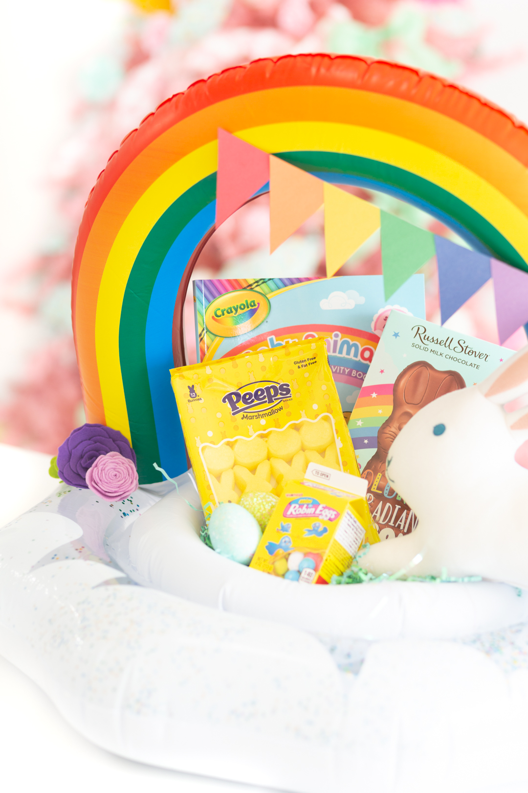 cute pool float easter basket that is rainbow themed, filled with matching items in rainbow colors such as yellow peeps, crayola coloring book, stuffed bunny