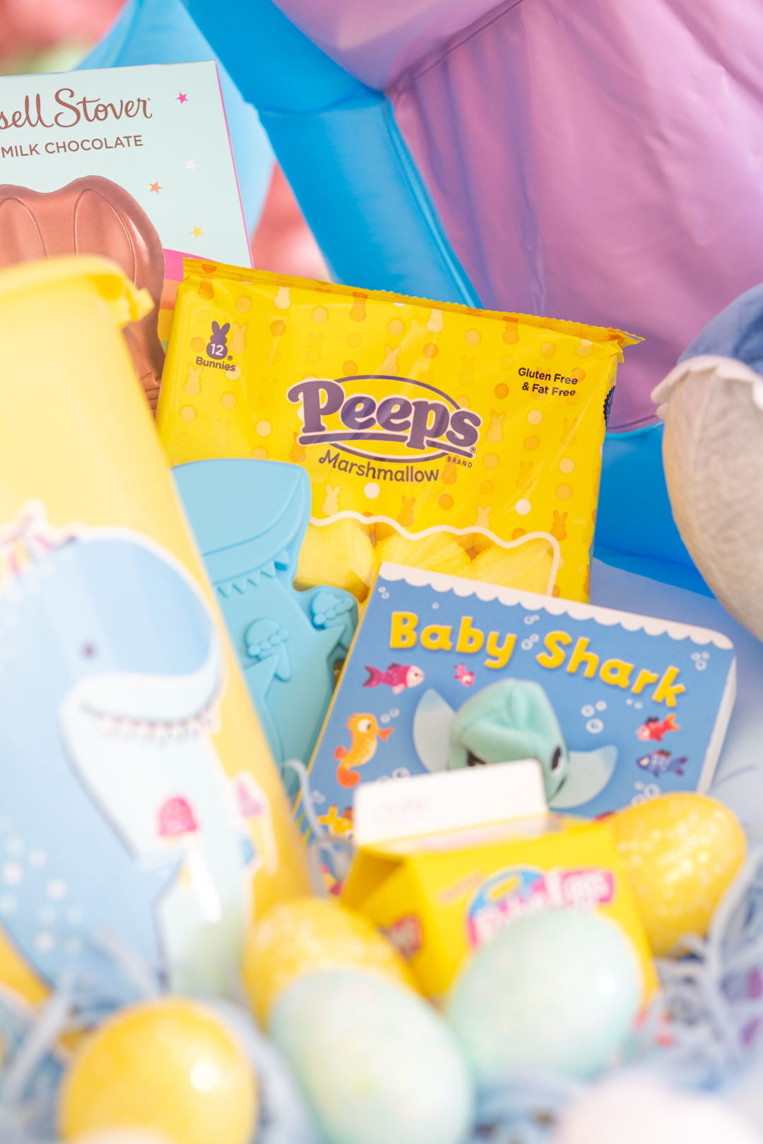 inside view of a big shark themed easter basket. Shark pail, yellow Peeps, baby shark book, plastic easter eggs.