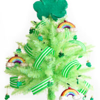 st. patrick's day tree using a mini lime green christmas tree with glass rainbow ornaments, green and white striped ribbon, mini shamrock ornaments and a mini shamrock piñata as a tree topper