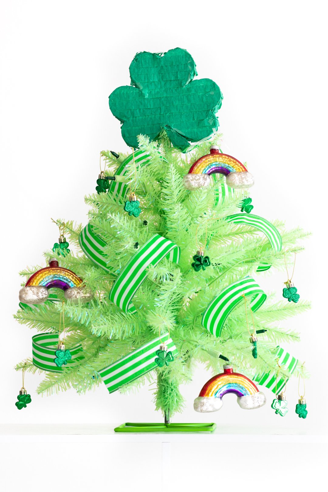 st. patrick's day tree using a mini lime green christmas tree with glass rainbow ornaments, green and white striped ribbon, mini shamrock ornaments and a mini shamrock piñata as a tree topper