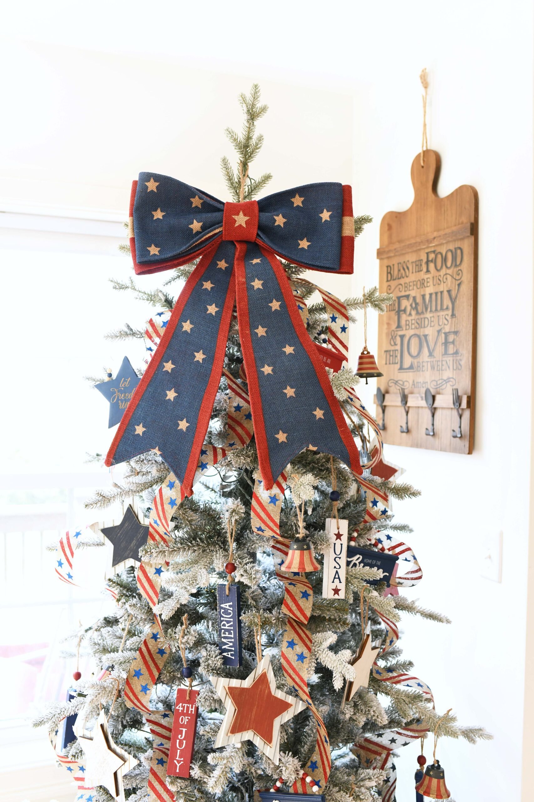 red white and clue christmas tree with a gigantic patriotic bow on top as a tree topper. Farmhouse flocked tree.