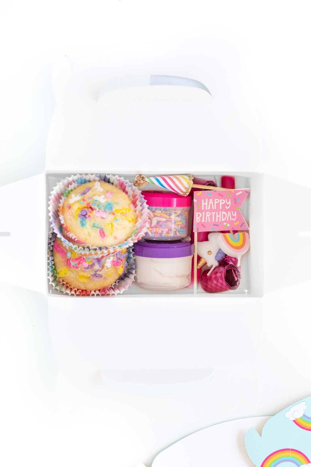 close up of items inside of a party favor box including funfetti style cupcakes, sprinkles and other birthday related trinkets