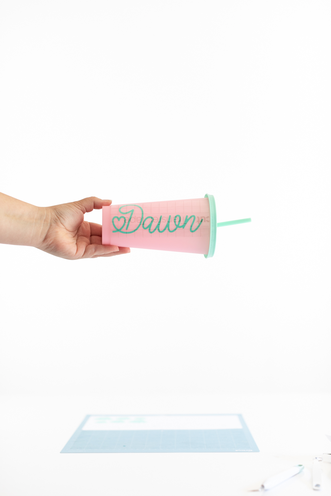 using craft scraper to press vinyl letters onto teal color changing tumbler