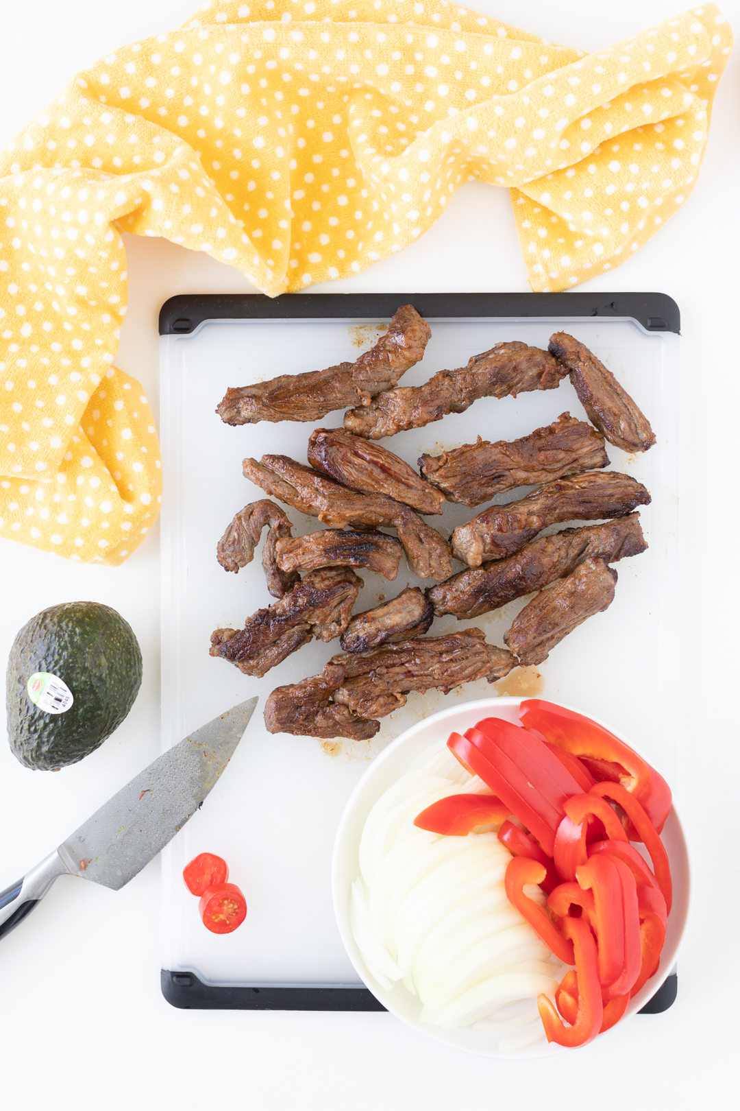 chopped steak strips on a cutting board with fresh cut peppers and onions nearby