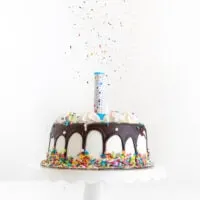 surprise candle loaded with edible confetti placed onto a simple birthday cake with a chocolate drip