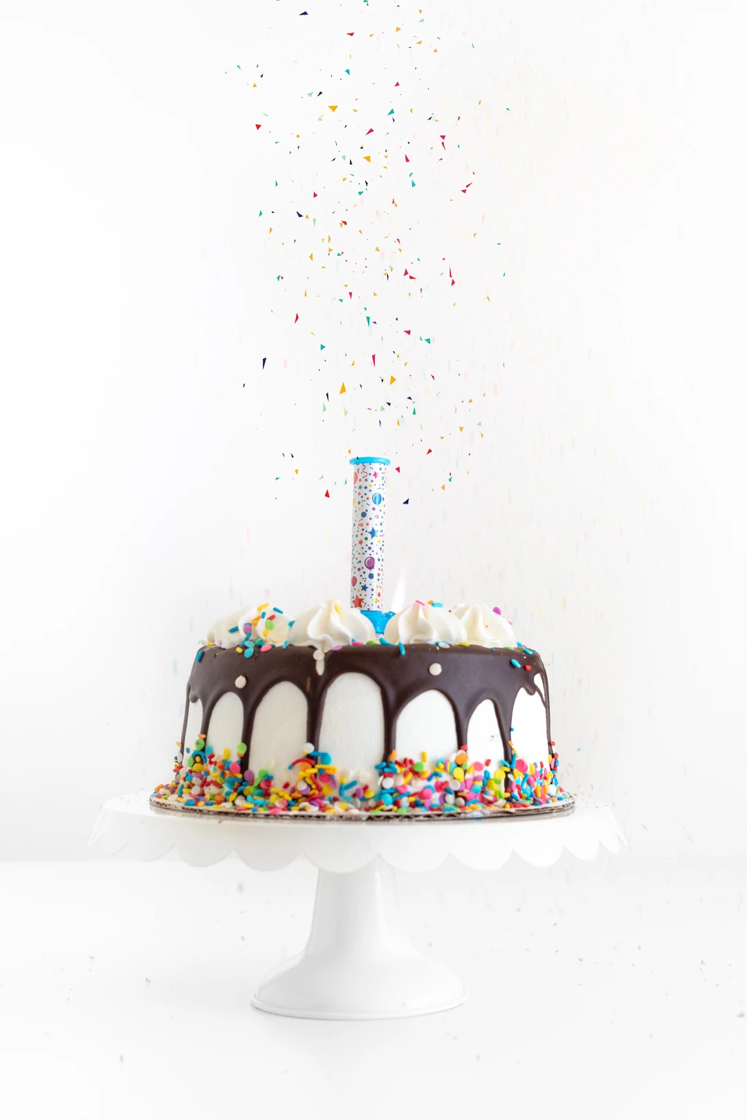 surprise candle loaded with edible confetti placed onto a simple birthday cake with a chocolate drip