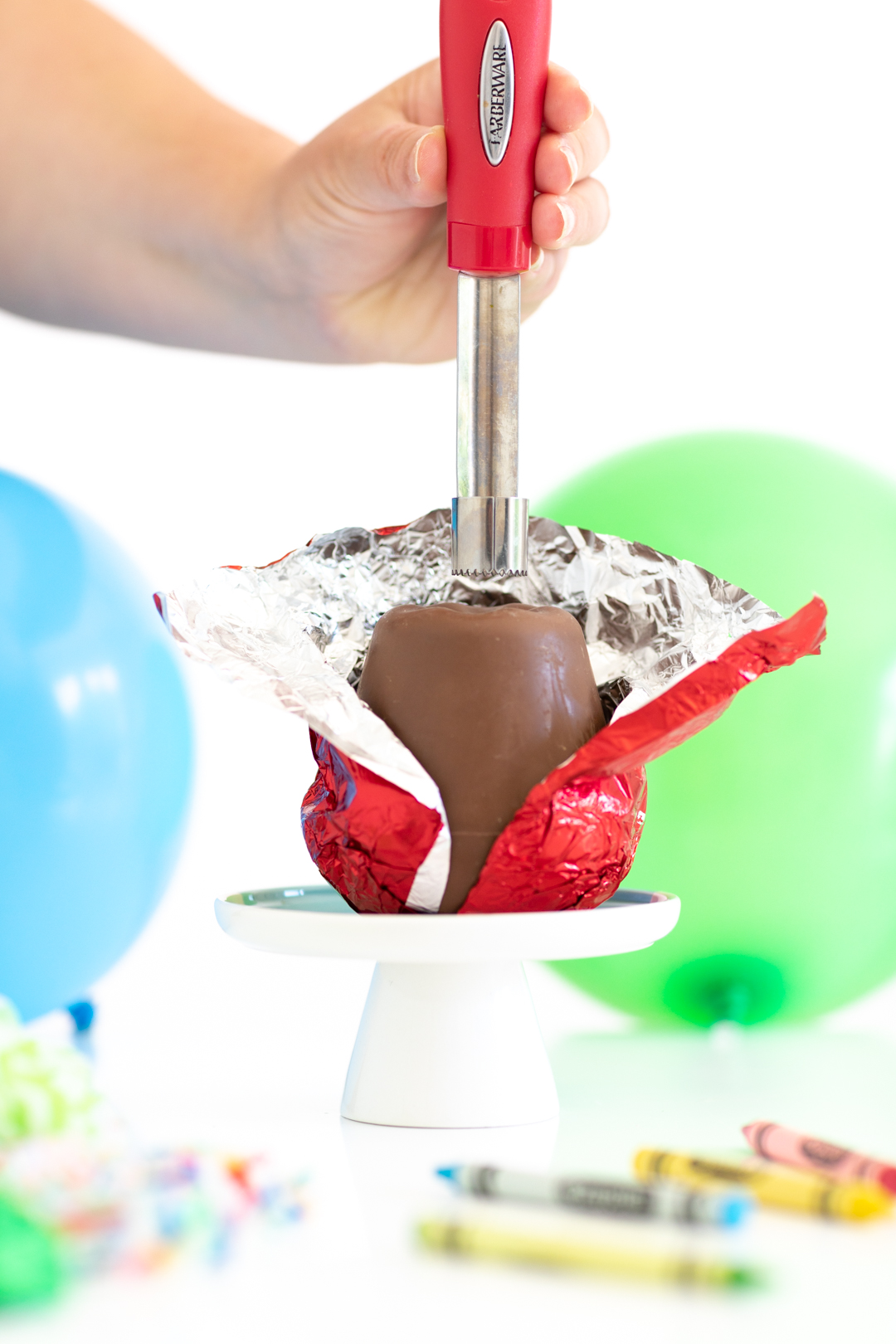 woman using a heated apple corer to poke a hole in a hollow chocolate apple.