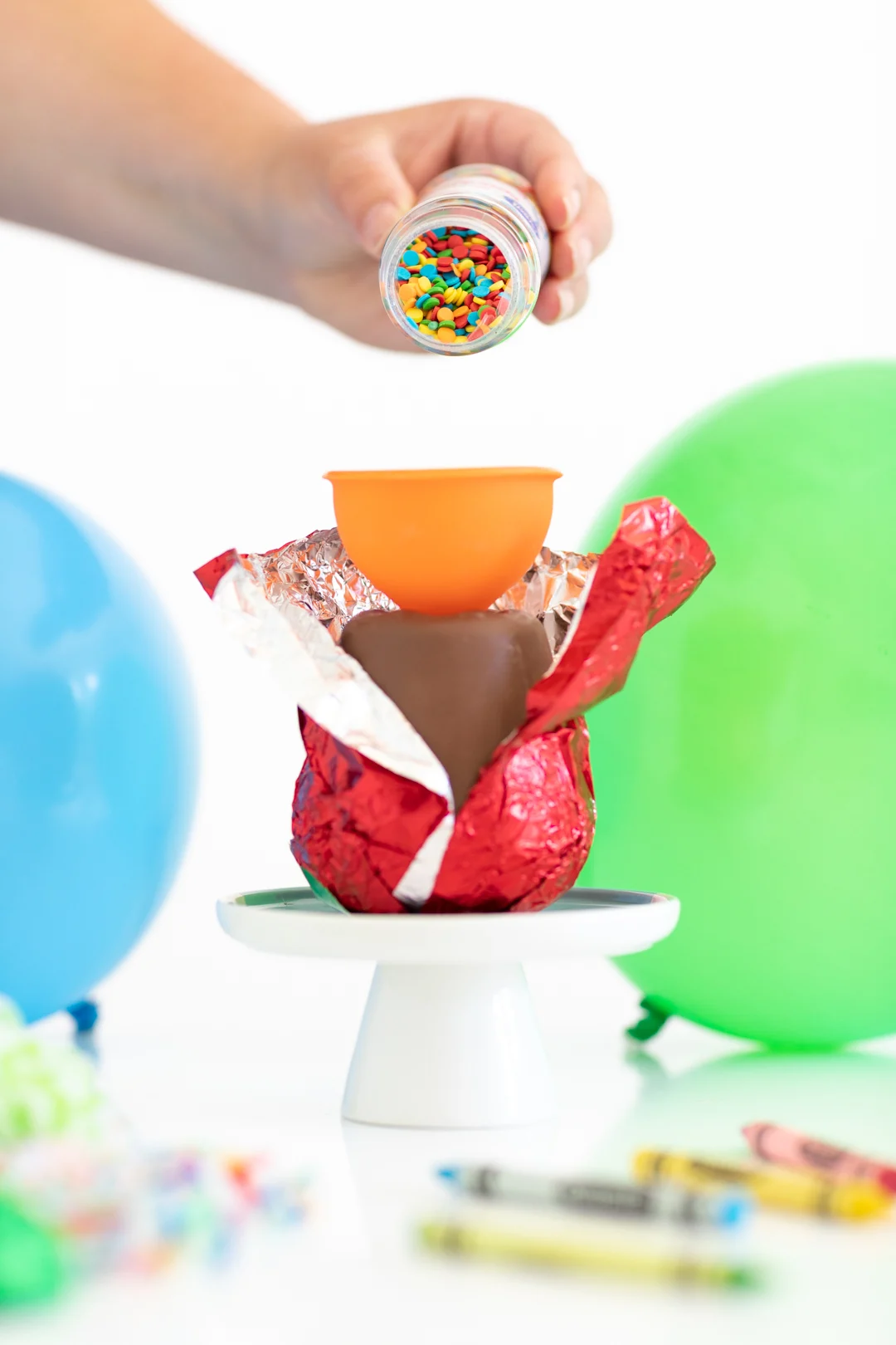woman pouring sprinkles into a food funnel to get sprinkles into a hollow chocolate apple