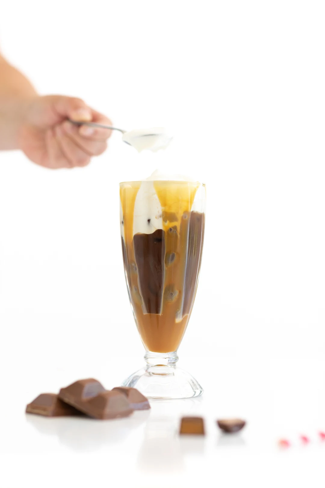 adding frothy cream to iced coffee in a glass
