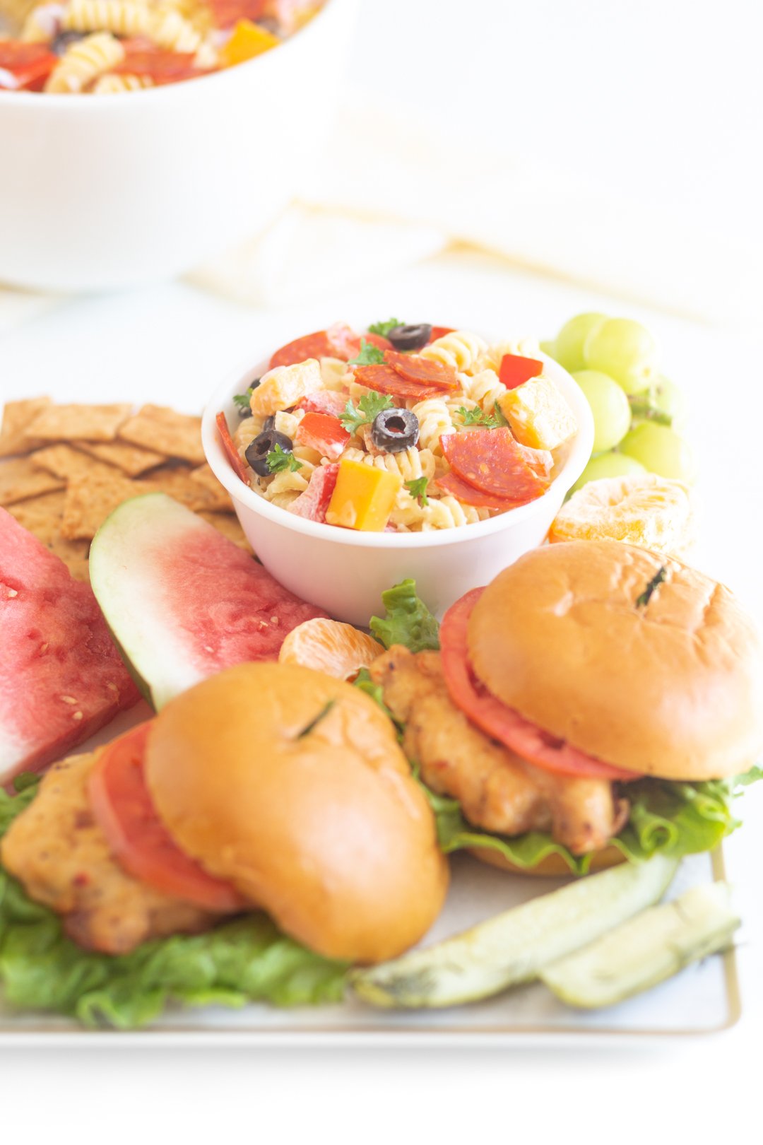 tray of barbecue items with chicken sandwiches, bowl of pasta salad, watermelon and more