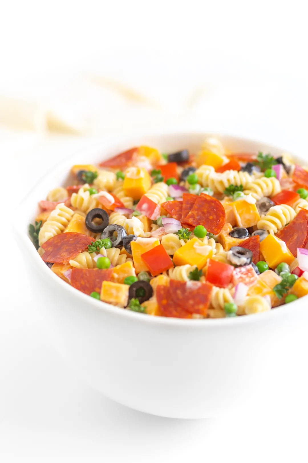 bowl of pasta salad with spiral pasta, pepperoni, black olives, onions