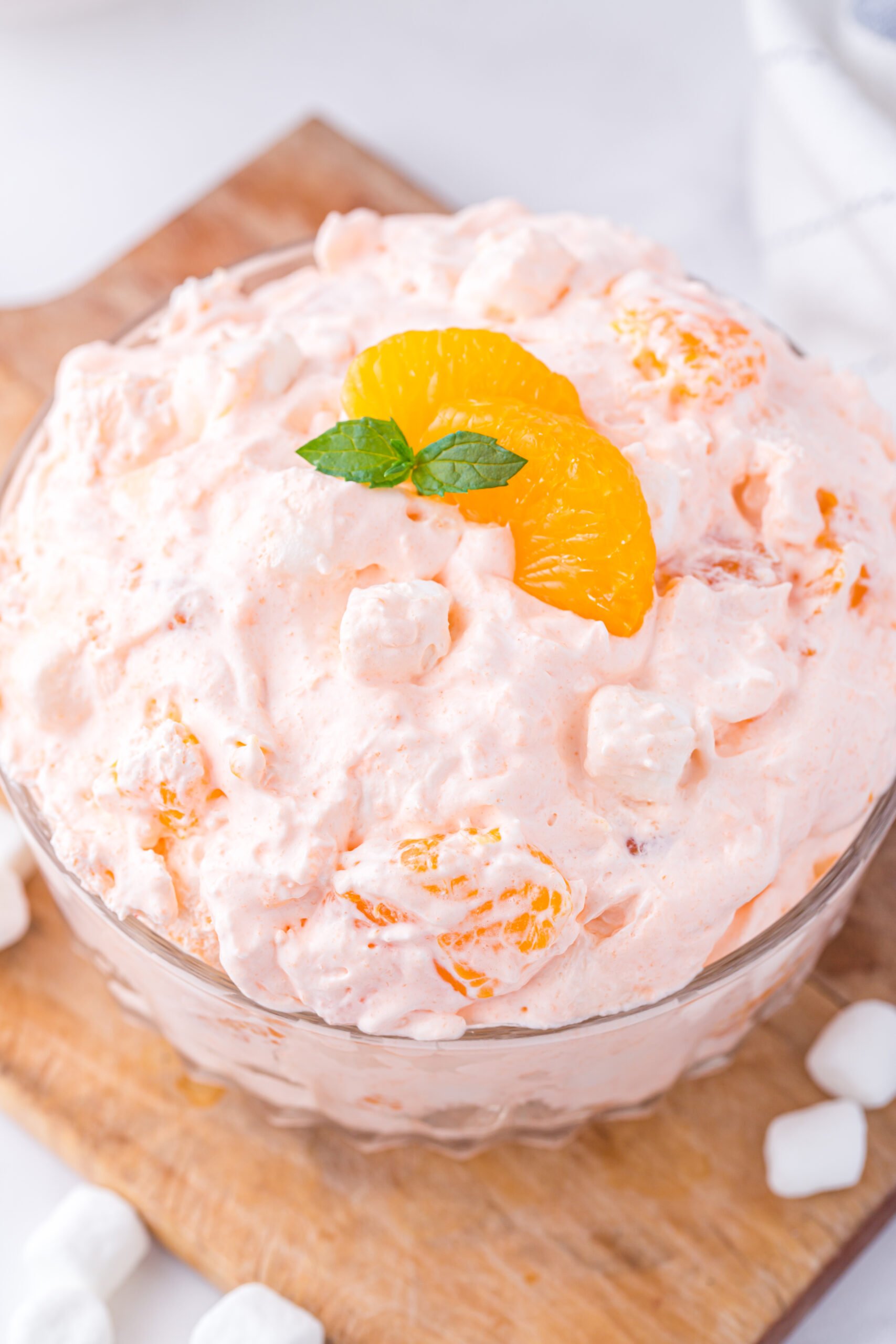 over the top view of a dish of orange fluff dessert. a slice of mandarin orange and fresh mint on top as garnish.