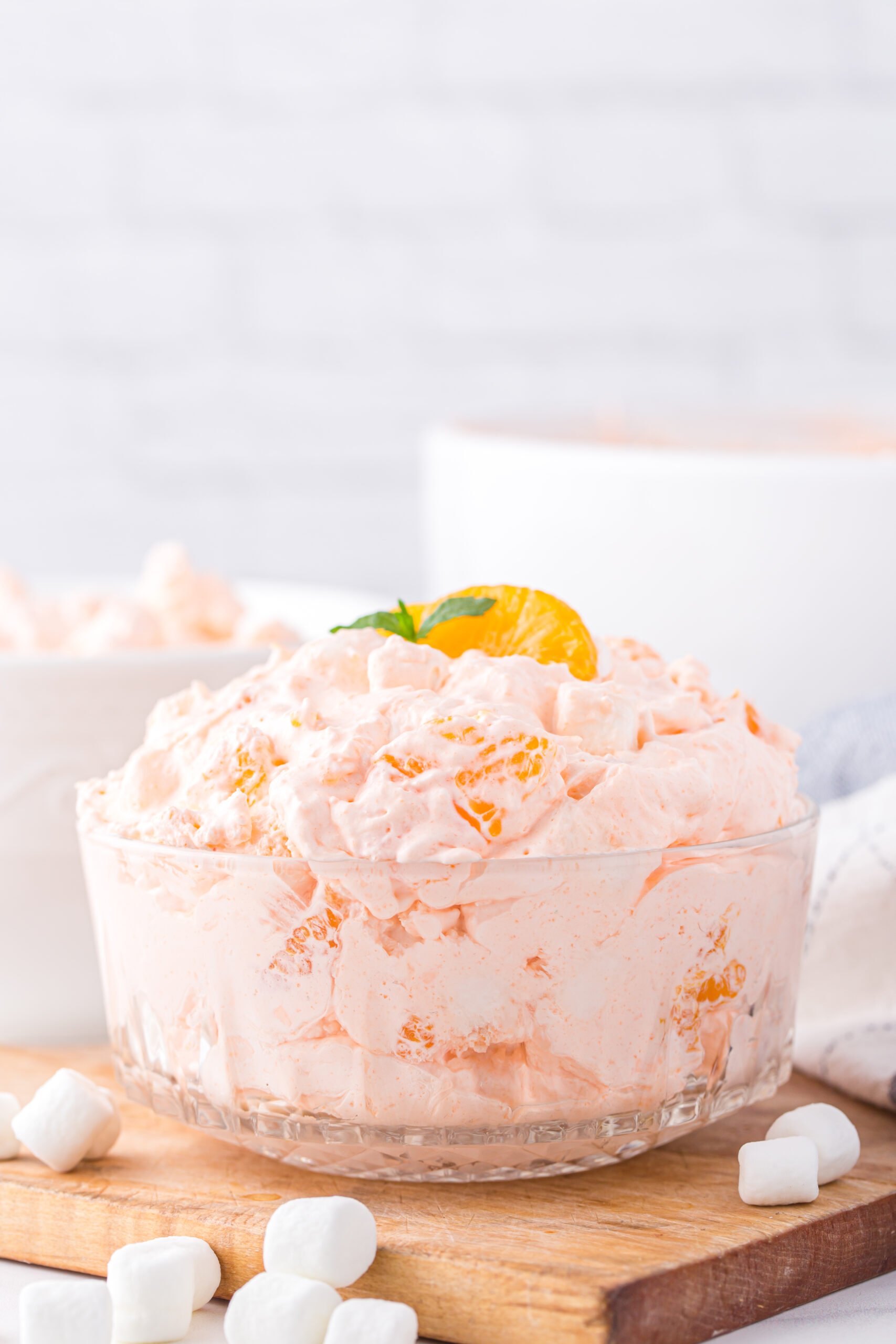 orange fluff whipped topping dessert in a bowl resting on a wooden cutting board with a white brick wall in the background