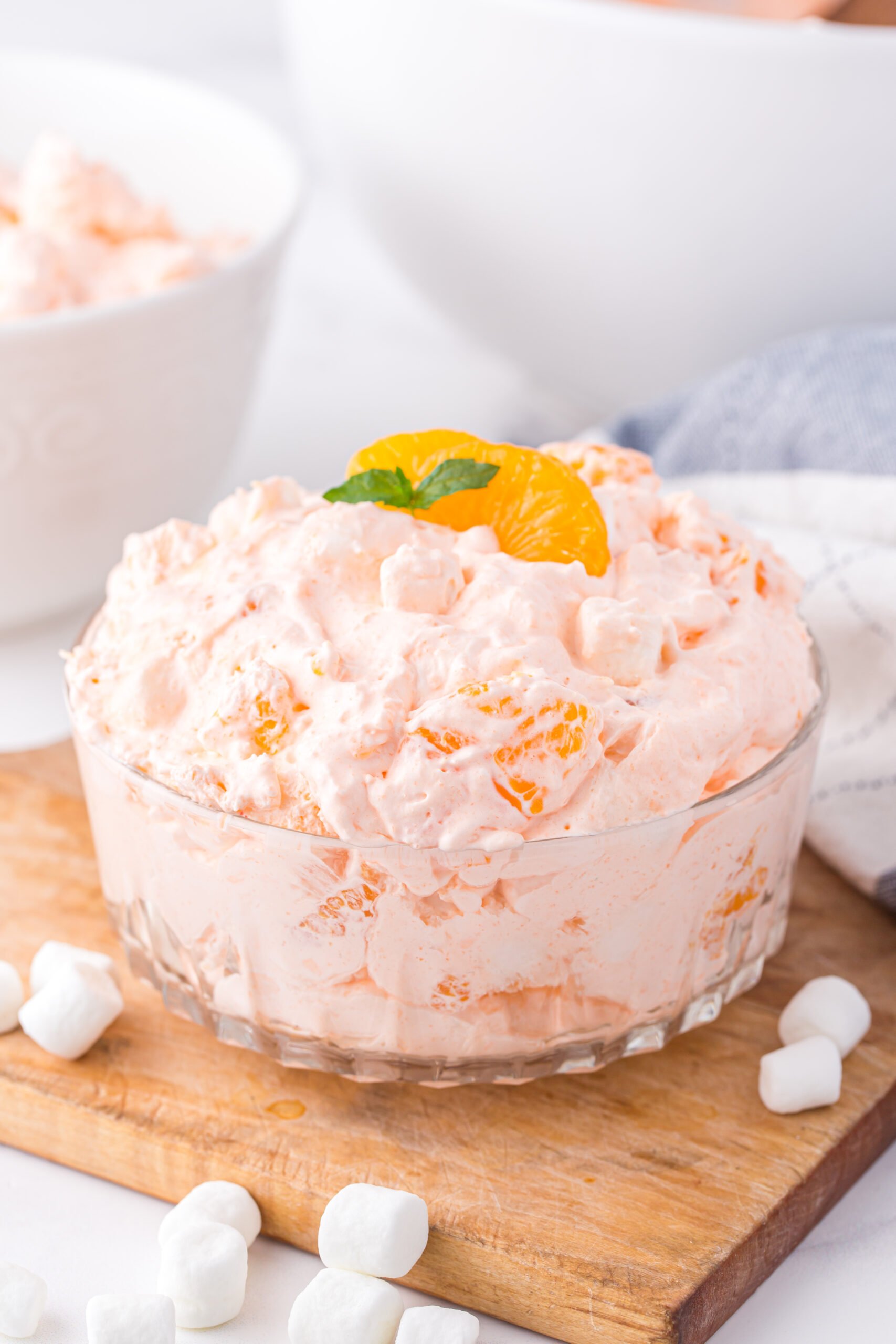 orange fluff dessert in a glass bowl with mandarin orange and fresh mint garnish