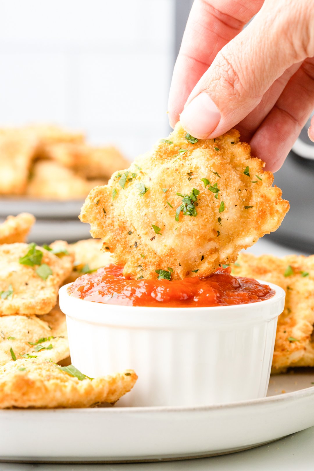 air fried ravioli being dipped into small bowl of marinara sauce