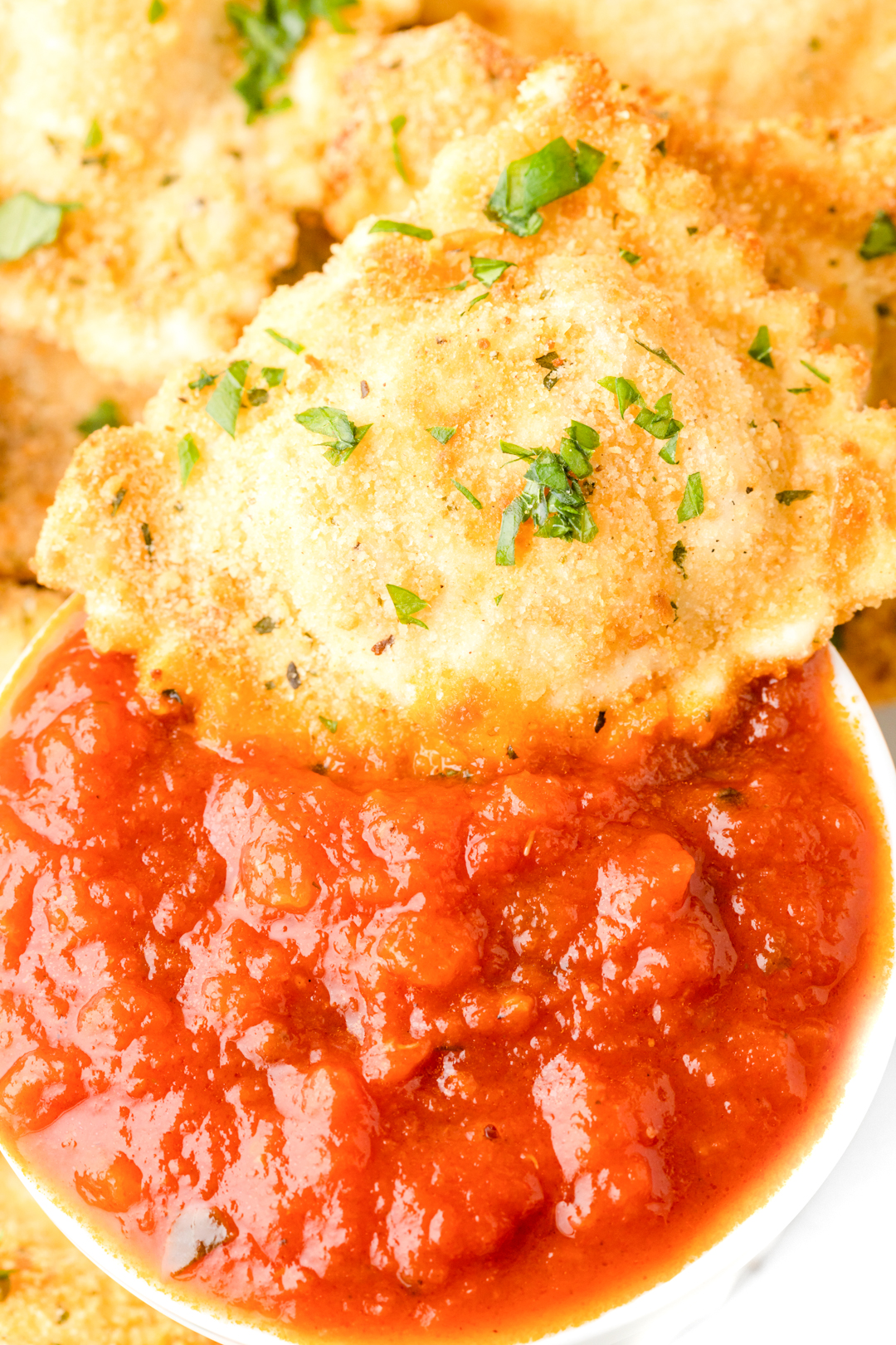 up close air fried ravioli being dipped into spaghetti sauce