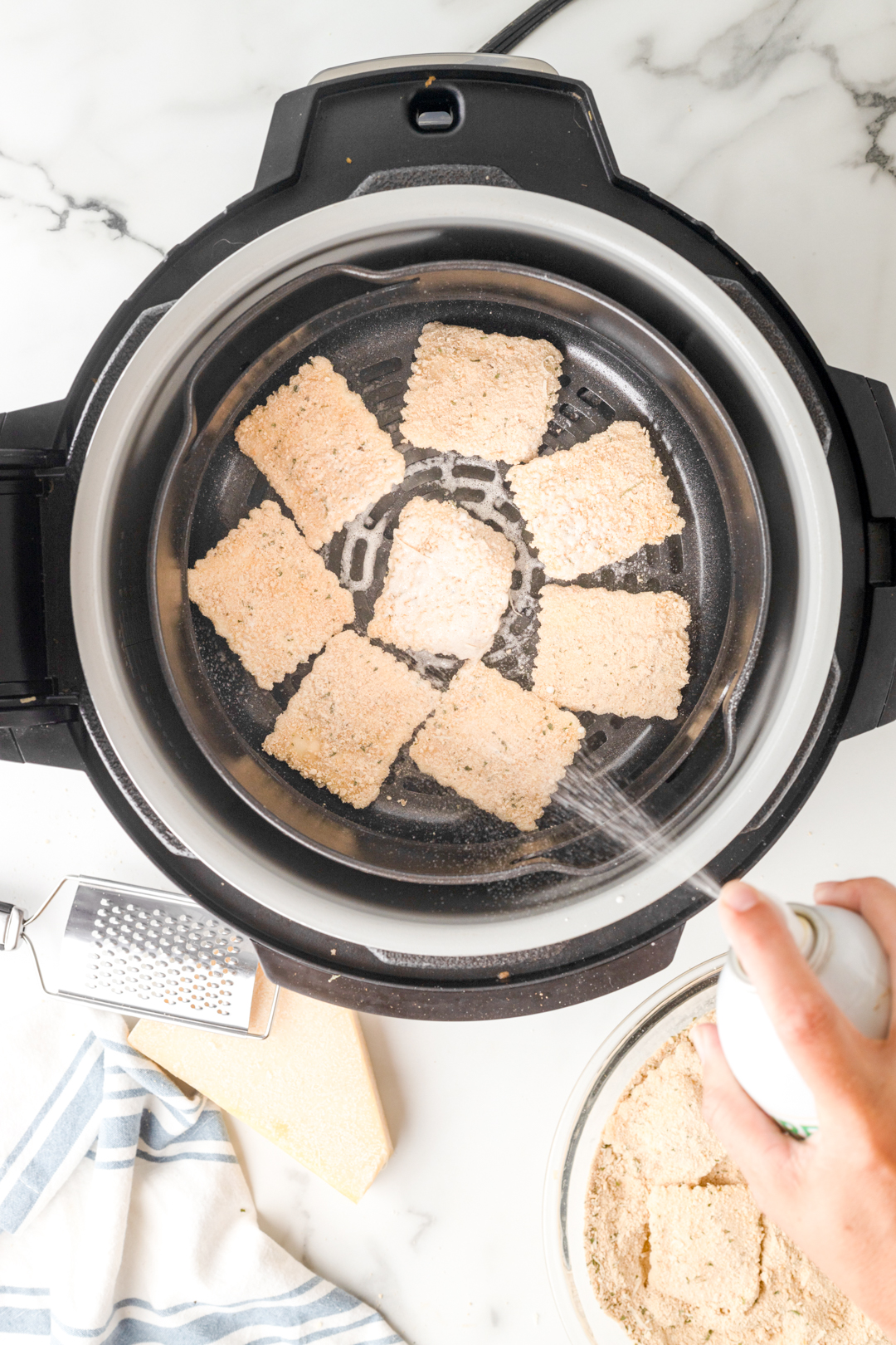 spraying breaded ravioli with nonstick spray in the airfryer