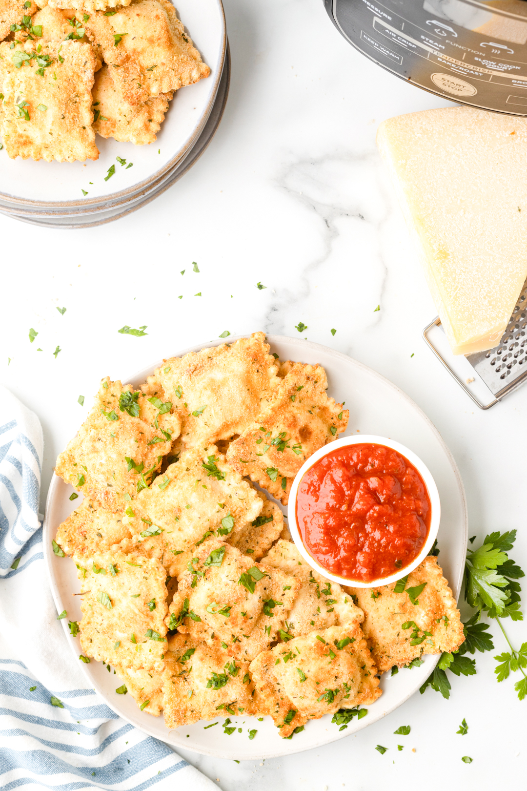 air fried ravioli on a small plate served next to a small dish of pasta sauce for dipping. Air fryer in the background.