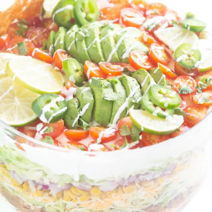 view of top of layered salad with sliced avocados, sliced cherry tomatoes and lime slices.