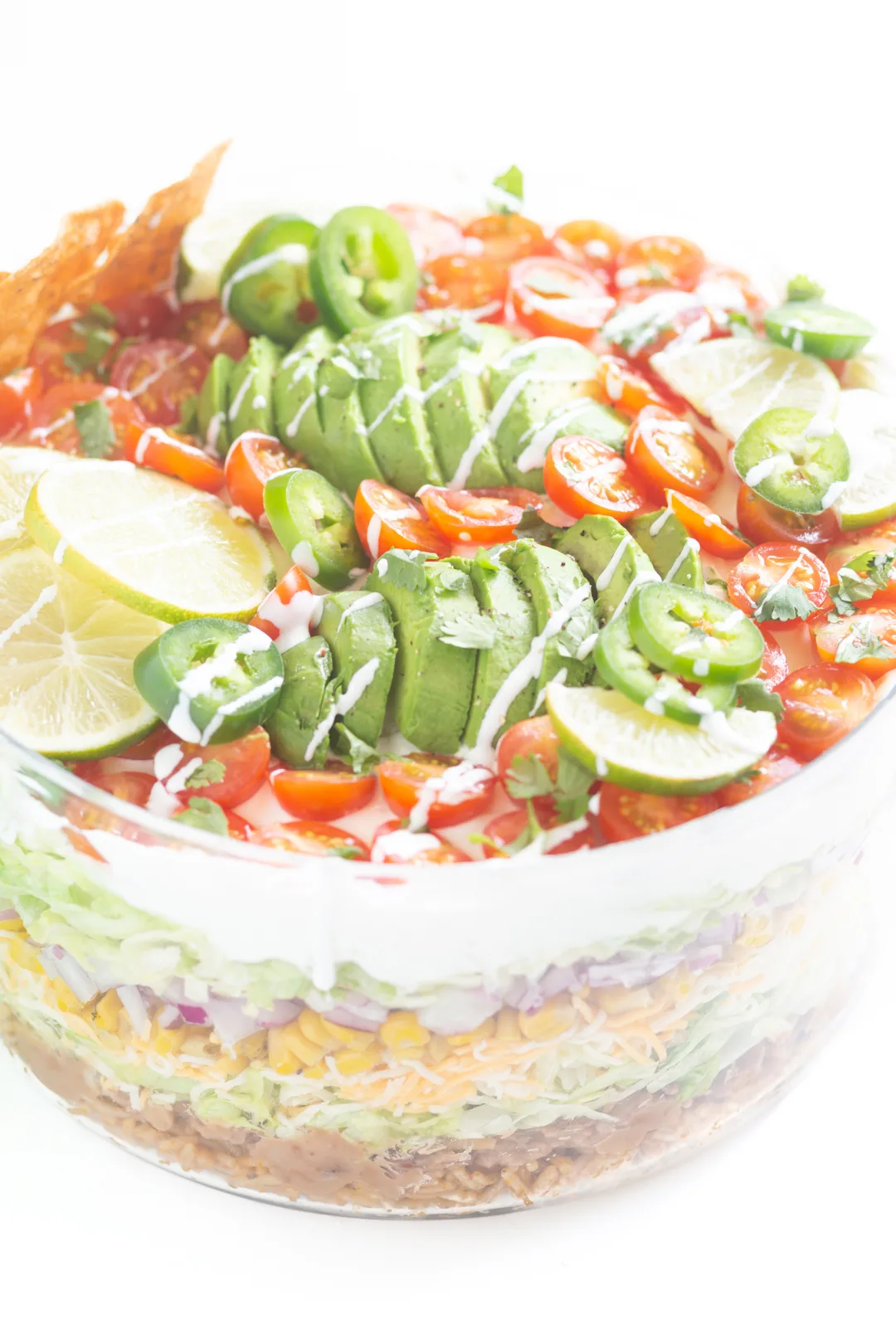 view of top of layered salad with sliced avocados, sliced cherry tomatoes and lime slices.