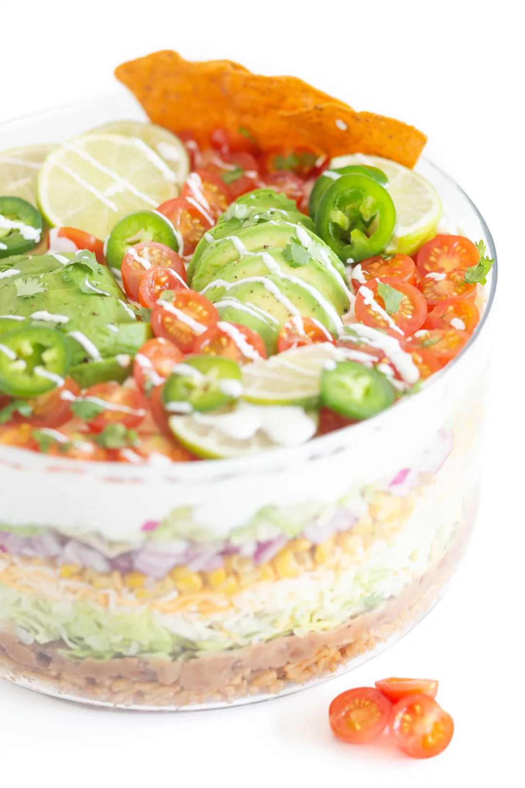 up close view of a pretty mexican layered salad topped with sliced avocado and halved cherry tomatoes, lime slices, cilantro
