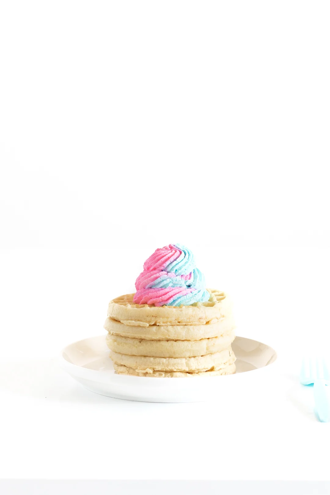 stack of waffles on a white plate with a lip topped with pink and blue swirled whipped cream