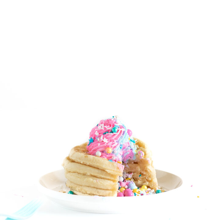 piñata waffle stack with pastel whipped cream on top and lots of sprinkles coming out of the center.