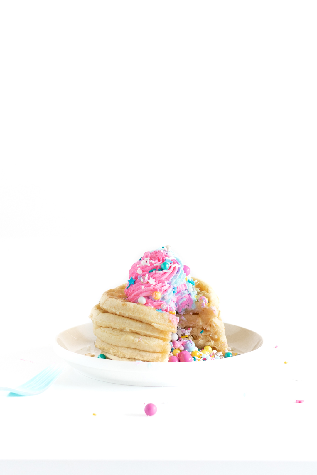 piñata waffle stack with pastel whipped cream on top and lots of sprinkles coming out of the center. 
