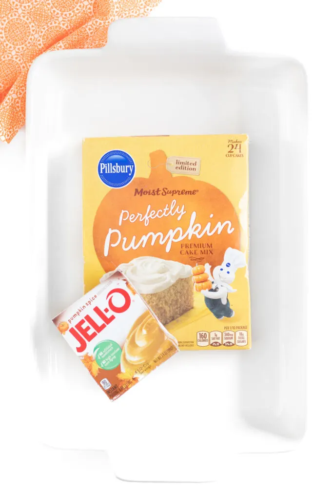 over the top photo of white baking dish with pillsbury perfectly pumpkin cake box and jello pumpkin spice instantly pudding mix box inside.