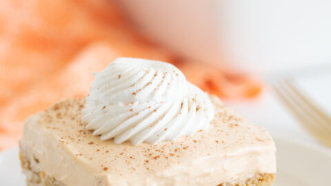 pumpkin ricotta cake on a small white plate with baking dish and orange cloth napkin in background