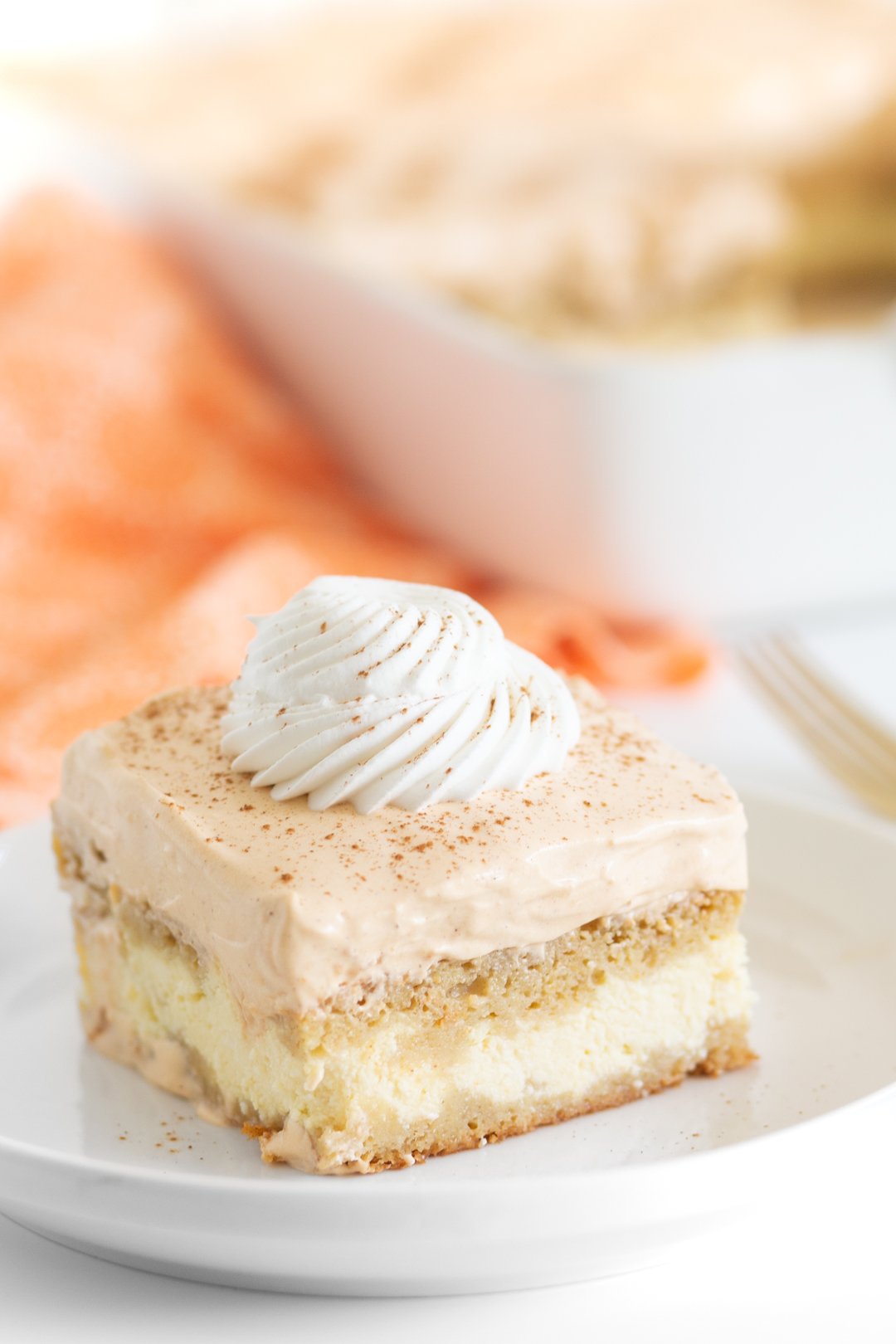 pumpkin ricotta cake on a small white plate with baking dish and orange cloth napkin in background