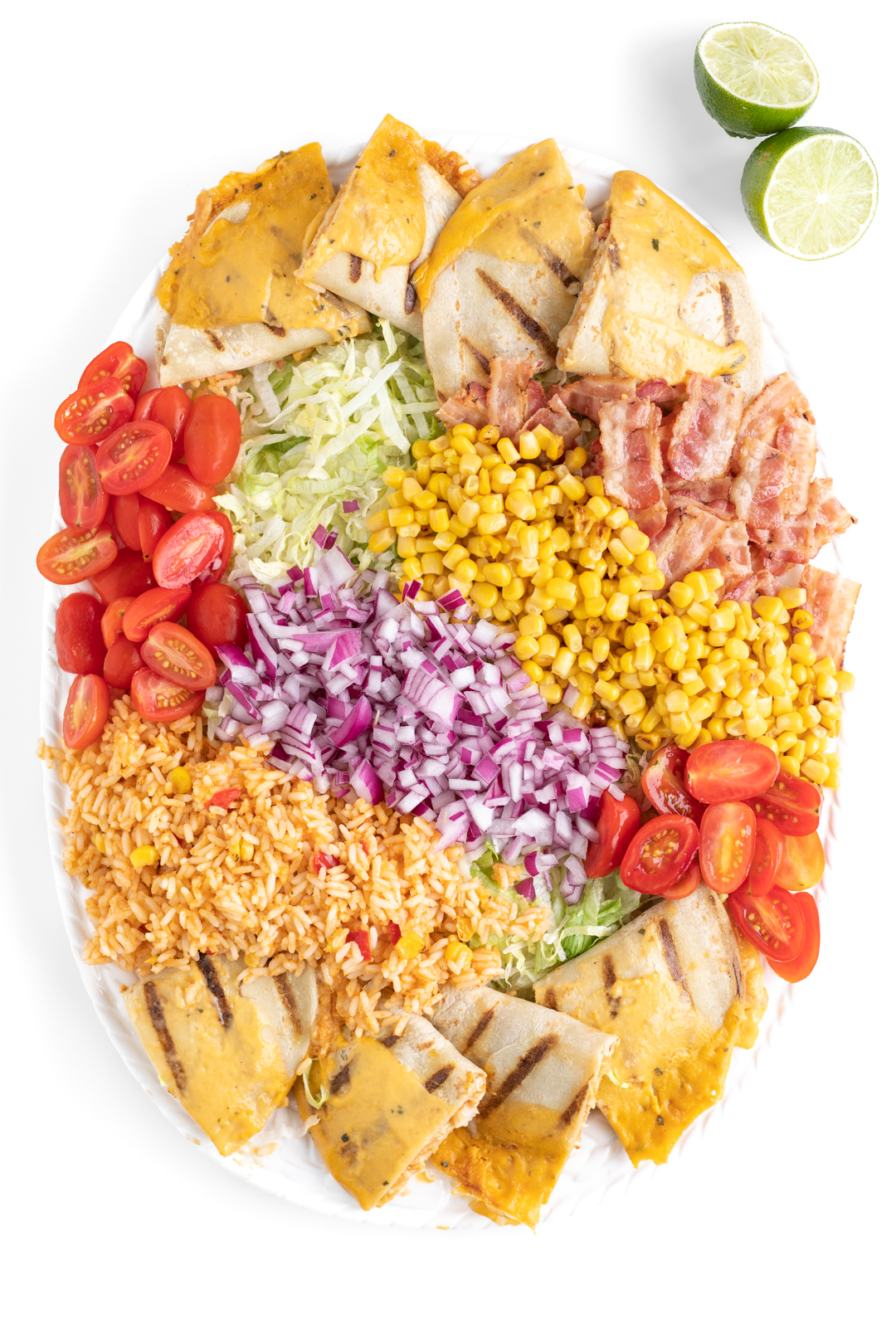 over top photo of a salad being made with shredded lettuce, grape tomatoes, mexican rice, bacon, quesadillas