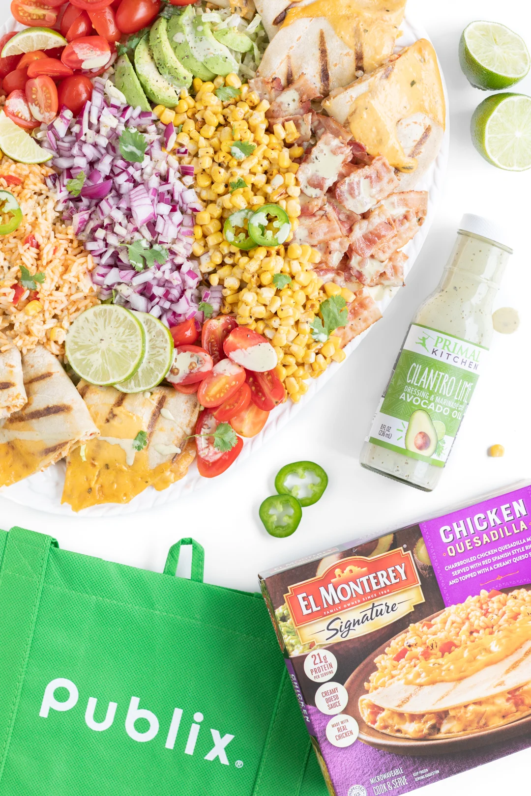 Over the top photo of large family salad, reusable publix shopping bag, el monterey quesadilla meal and primal kitchen lime and cilantro dressing
