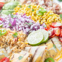close up of mexican inspired salad with chopped onions, sliced limes, quesadillas, halved grape tomatoes, lime