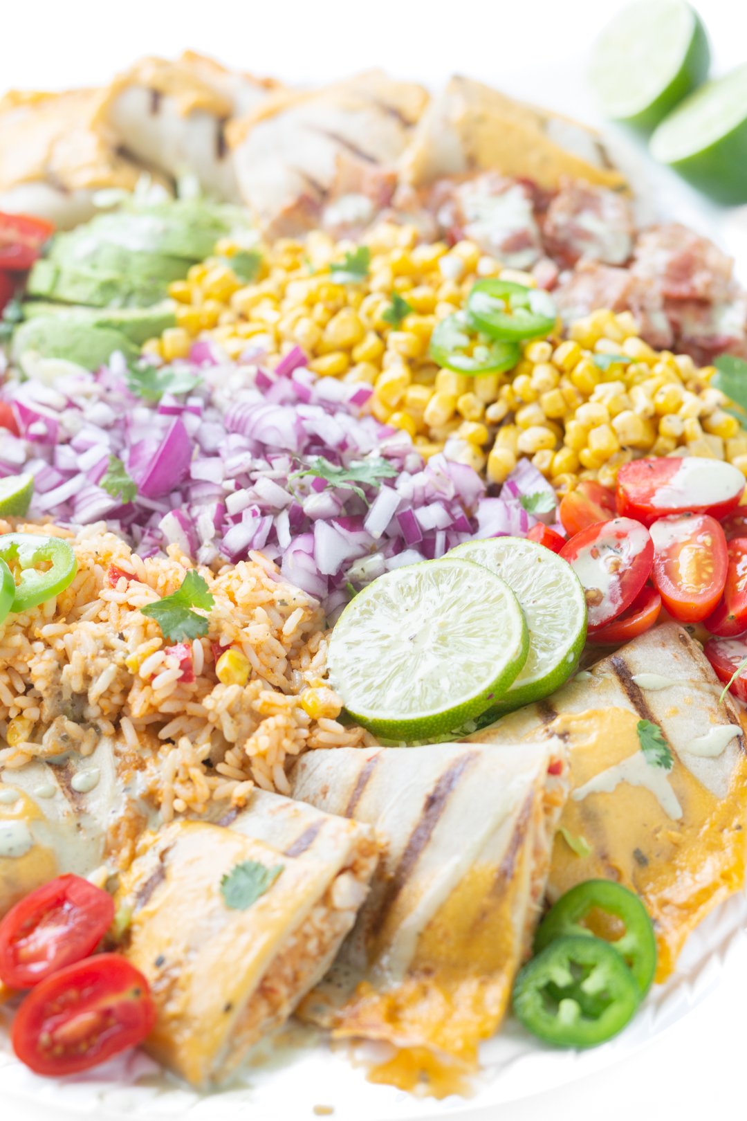 close up of mexican inspired salad with chopped onions, sliced limes, quesadillas, halved grape tomatoes, lime