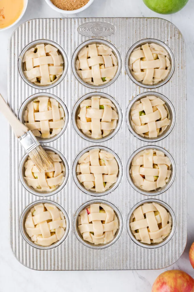 brushing on egg wash over mini pies in a muffin tin