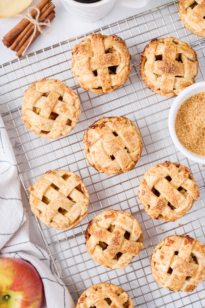 little apple pies set out on a cooking rack with sugar and cinnamon in bowl next to it