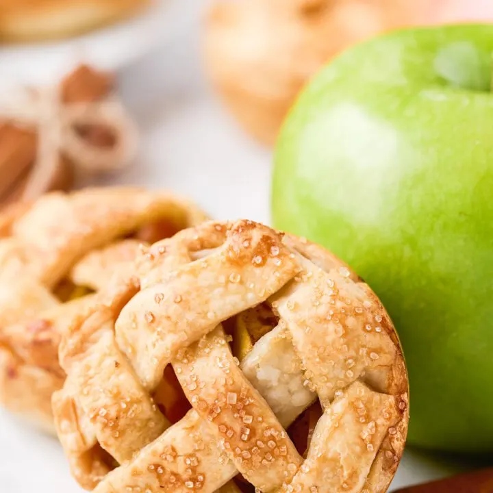 pretty little apple pies resting against a green apple