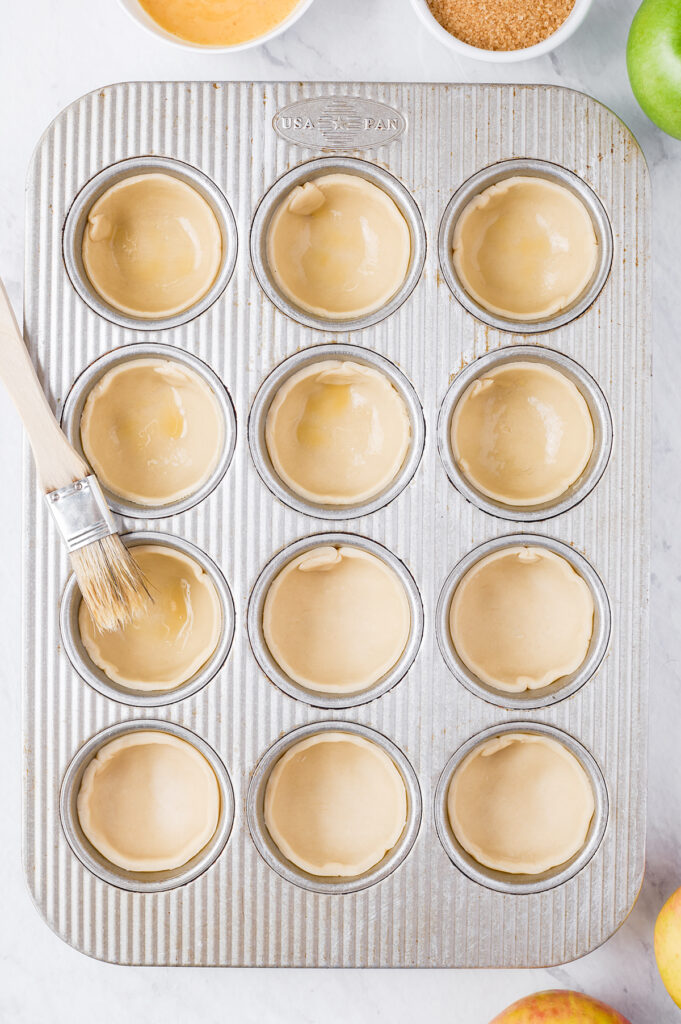 brushing egg wash onto dough pressed into a muffin tin