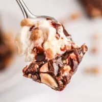 bite of thin brownie and ice scream on fork with peanuts and chocolatey drizzle