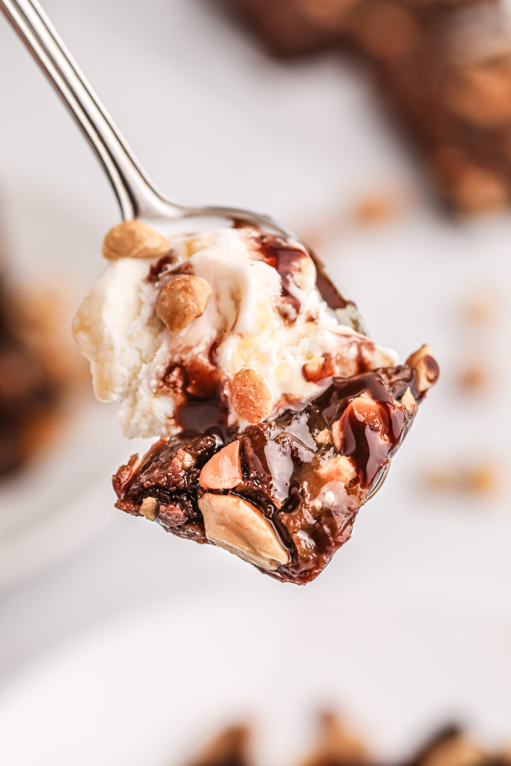 bite of thin brownie and ice scream on fork with peanuts and chocolatey drizzle