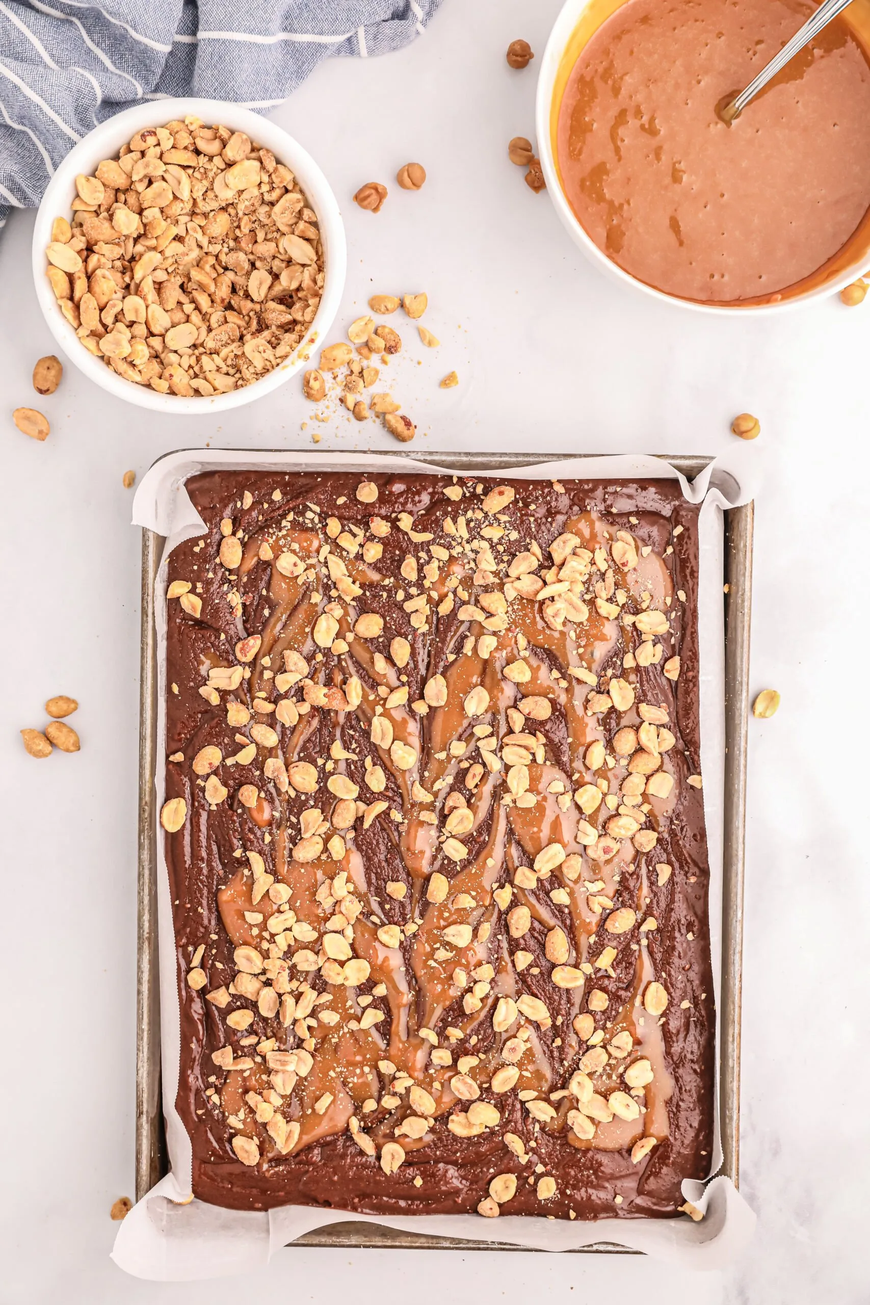 caramel swirl and peanuts topping a brownie batter in a sheet pan