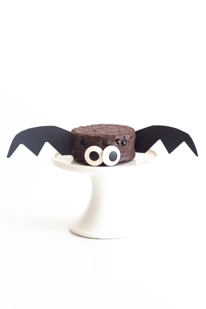 chocolate snack cake decorated like a bat with big candy eyes and black wings cut out of thick black paper.