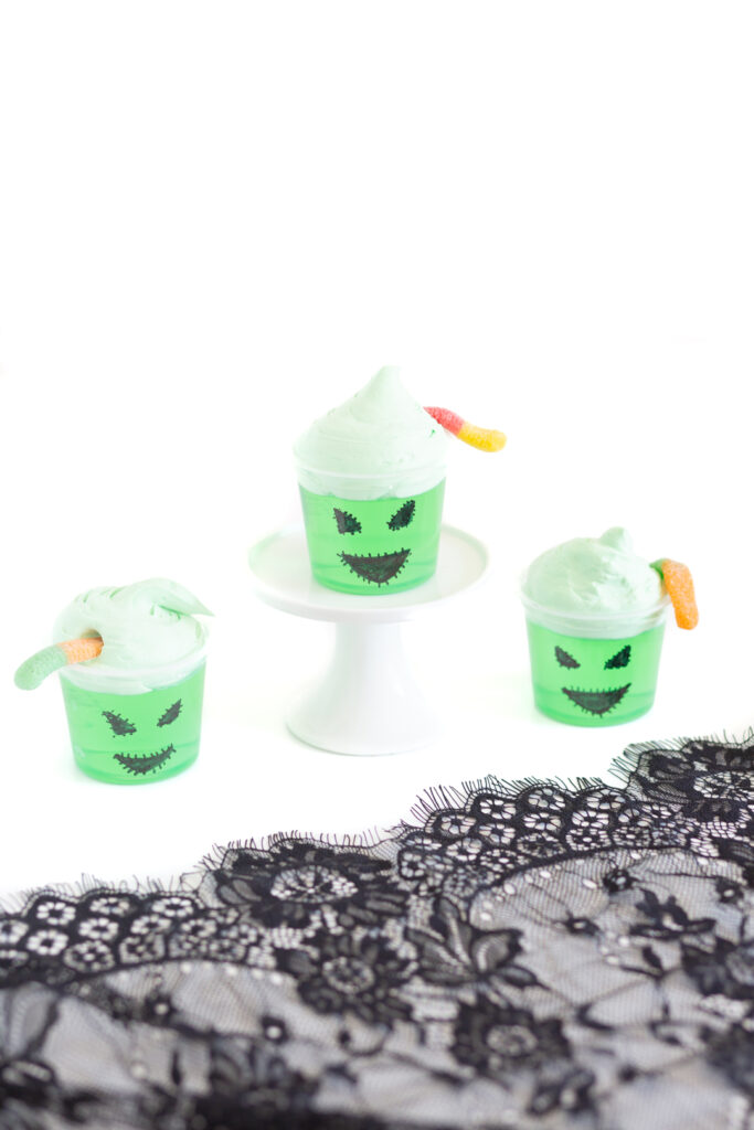 halloween jello cups decorated to look like oogie boogie with black sharpe and tinted cool whip.