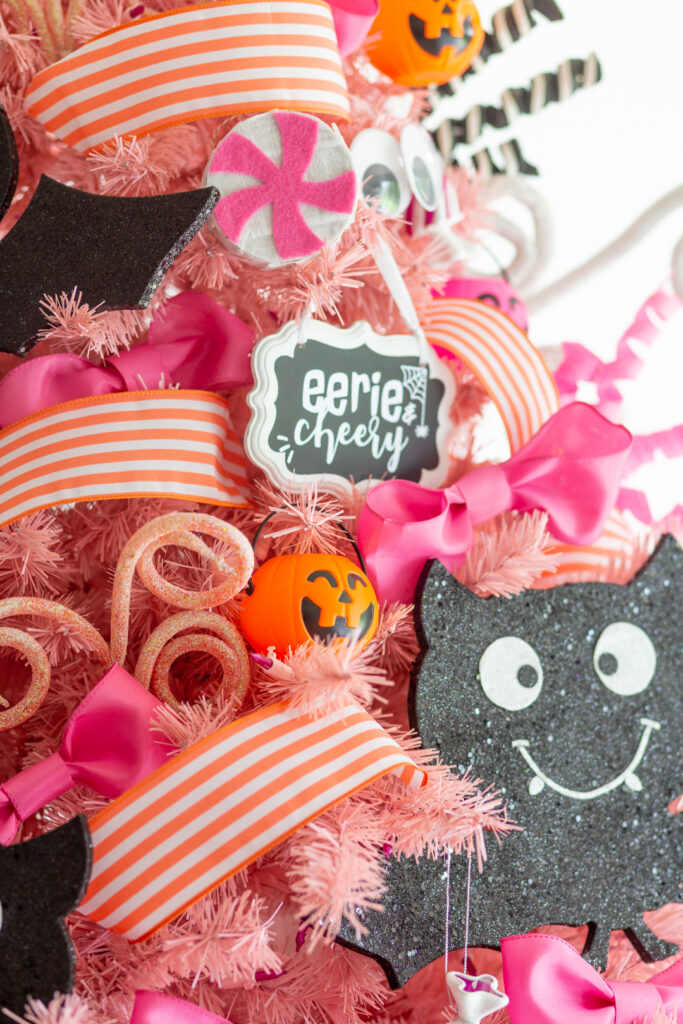 close up view of pink christmas tree with mini pumpkin treat bucket ornaments, giant bat ornaments, pink bow, mini pinatas