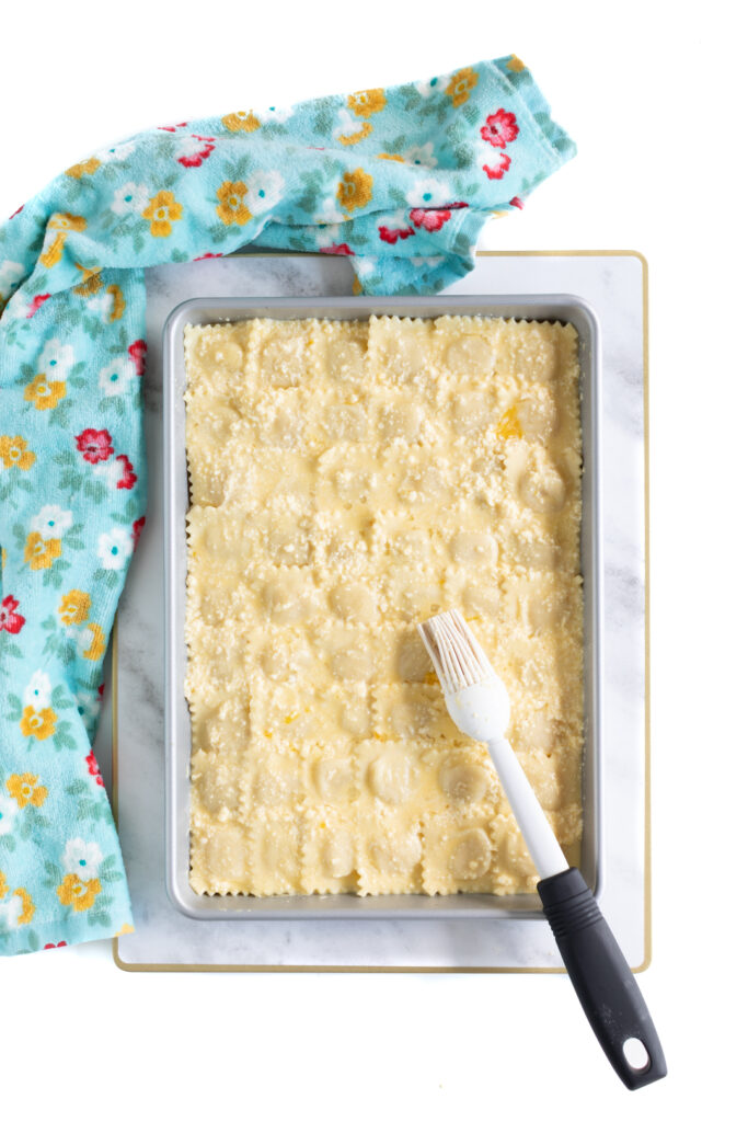 adding egg wash to ravioli based pizza crust on a half baking sheet with a food brush